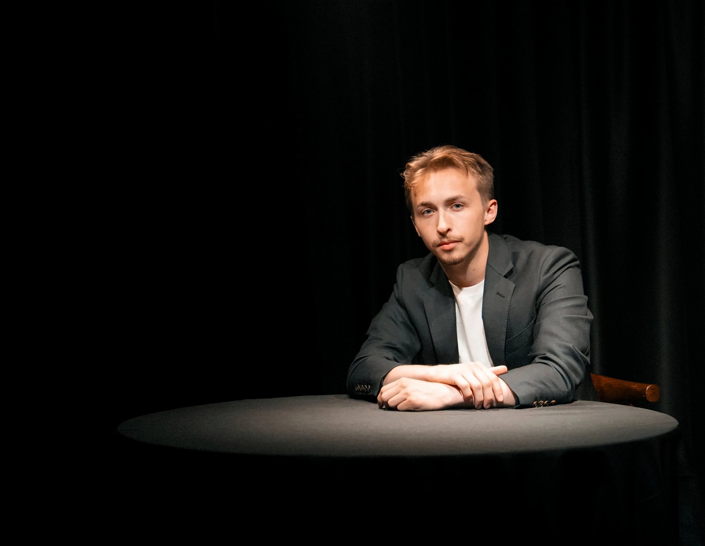 Tom Gibney seated at a round black table under a single spotlight