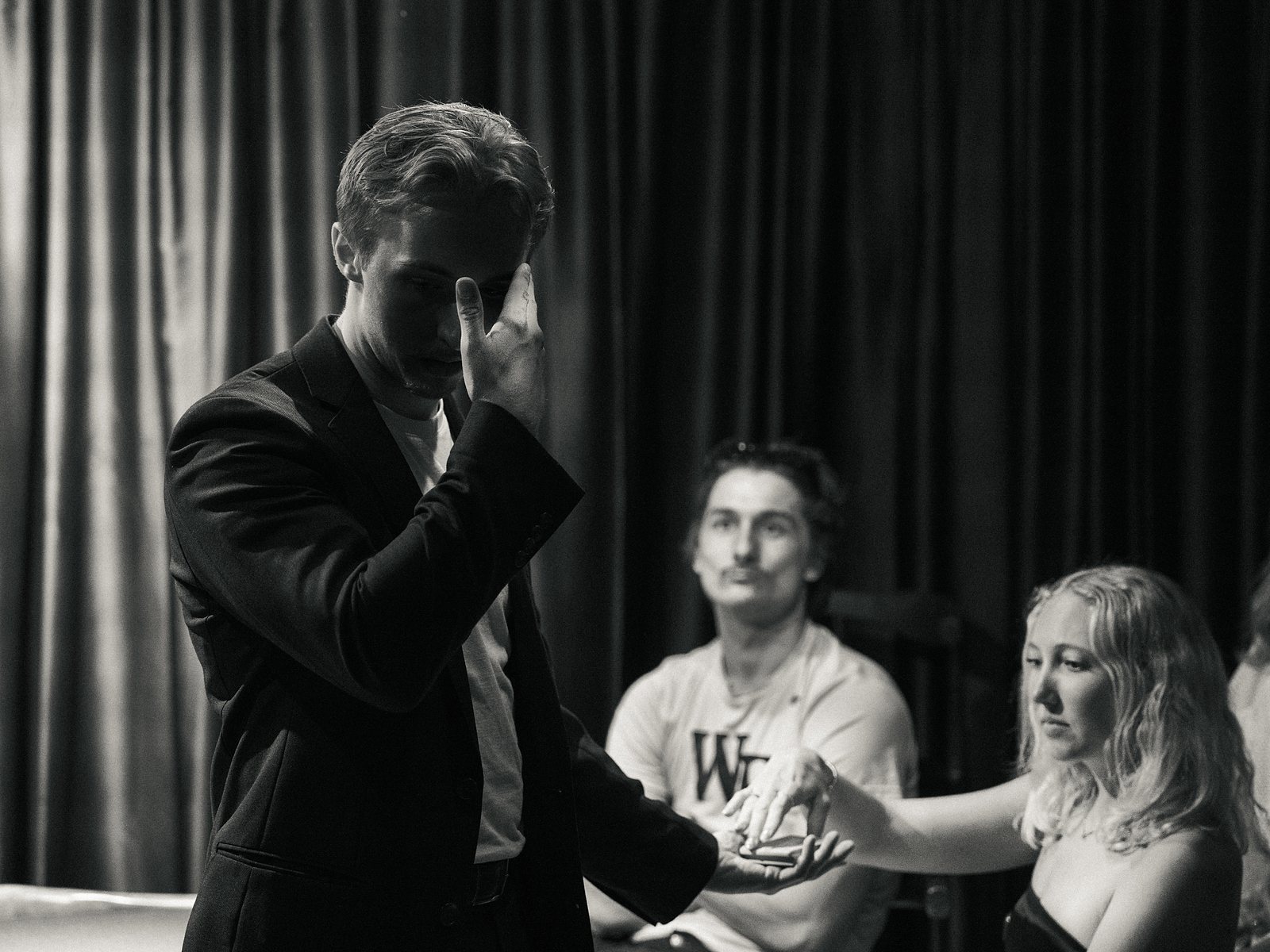 Tom mid-reveal in black and white as two guests look on