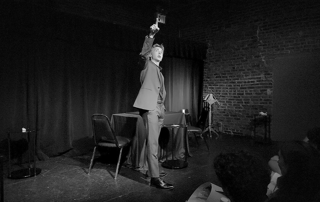 Tom pointing skyward on a black-box stage
